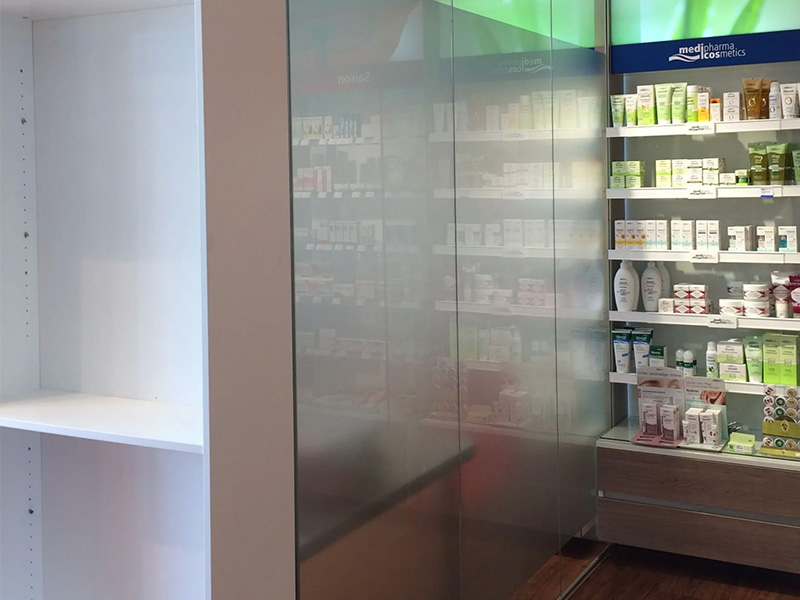Glastrennwand mit teilweiser Satinierung in Apotheke, Schiebetürsystem, Holzfußboden, beleuchtete Regale; moderne, funktionale Glaswände in Kiel. 